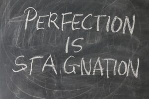 A picture of a blackboard showing the saying "perfection is stagnation" to illustrate a blog post on self sabotage on Nick Hughes coaching