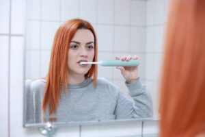 A picture of a woman brushing her teeth to show that habits conserve mental energy. It's being used in a blog on Nick Hughes Coaching talking about how willpower is a finite resource